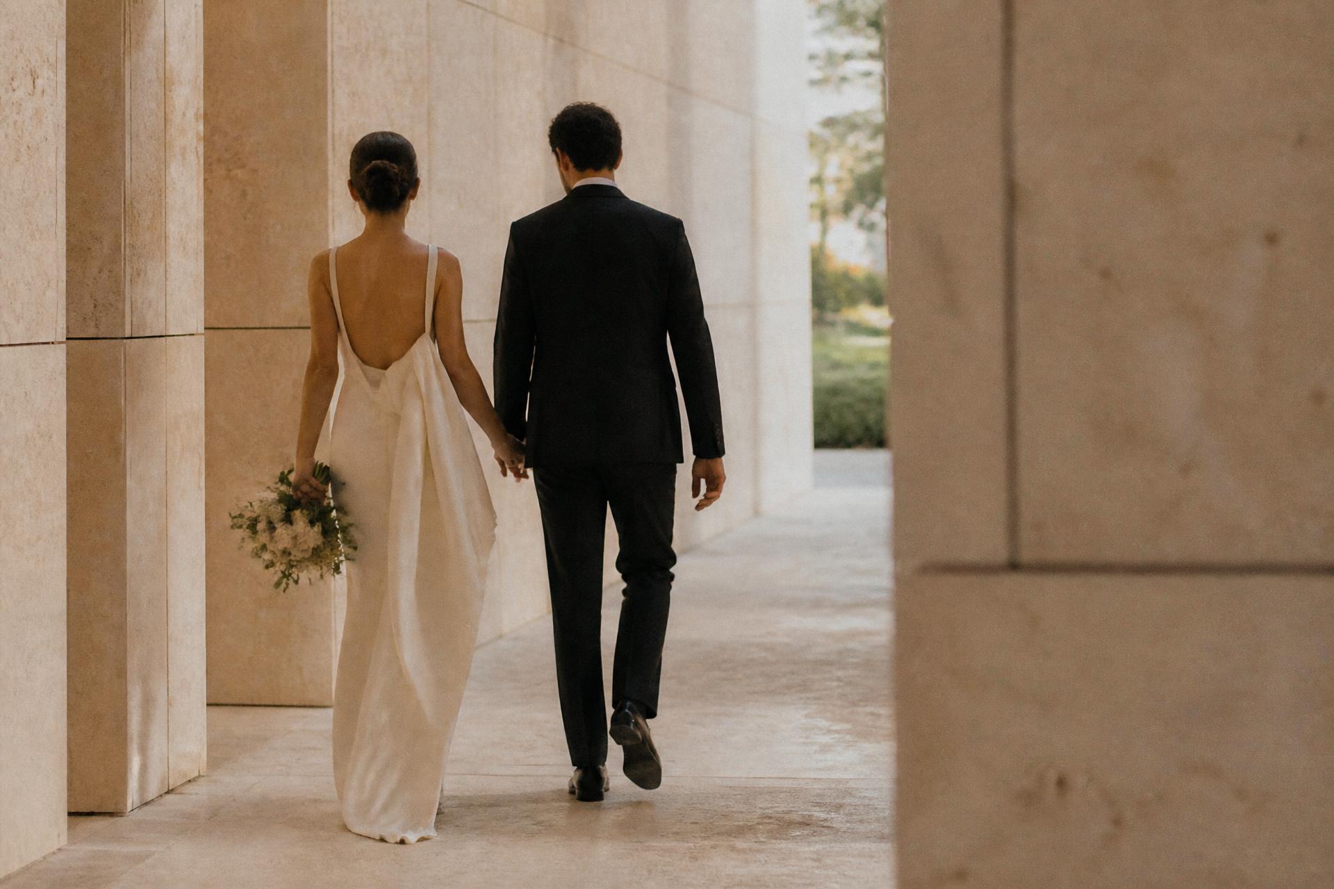 Bride and groom walking through a limestone corridor at golden hour